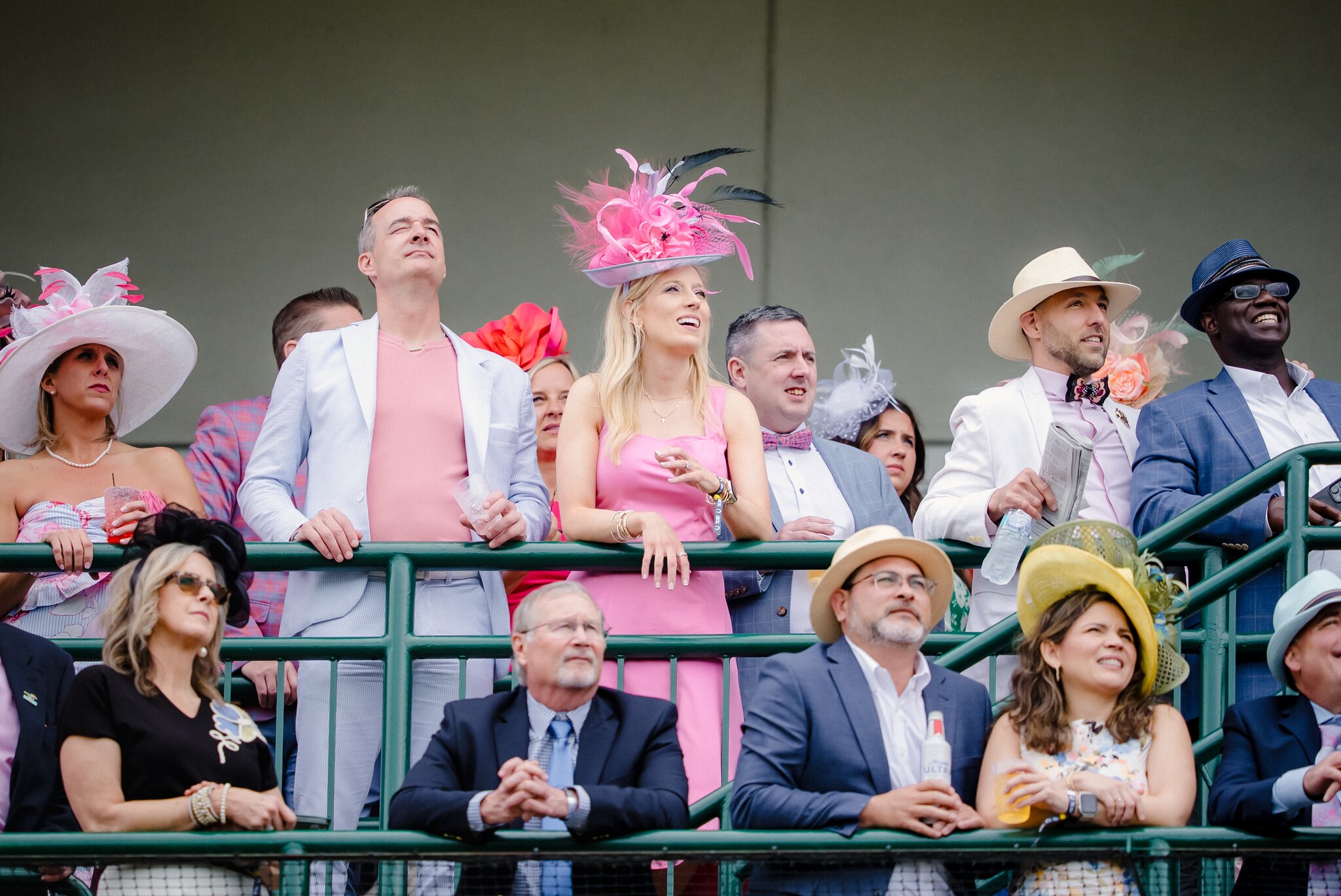 Spectators dressed in vibrant Derby fashion, featuring colorful suits and elaborate hats, watch the races from the grandstand at Churchill Downs