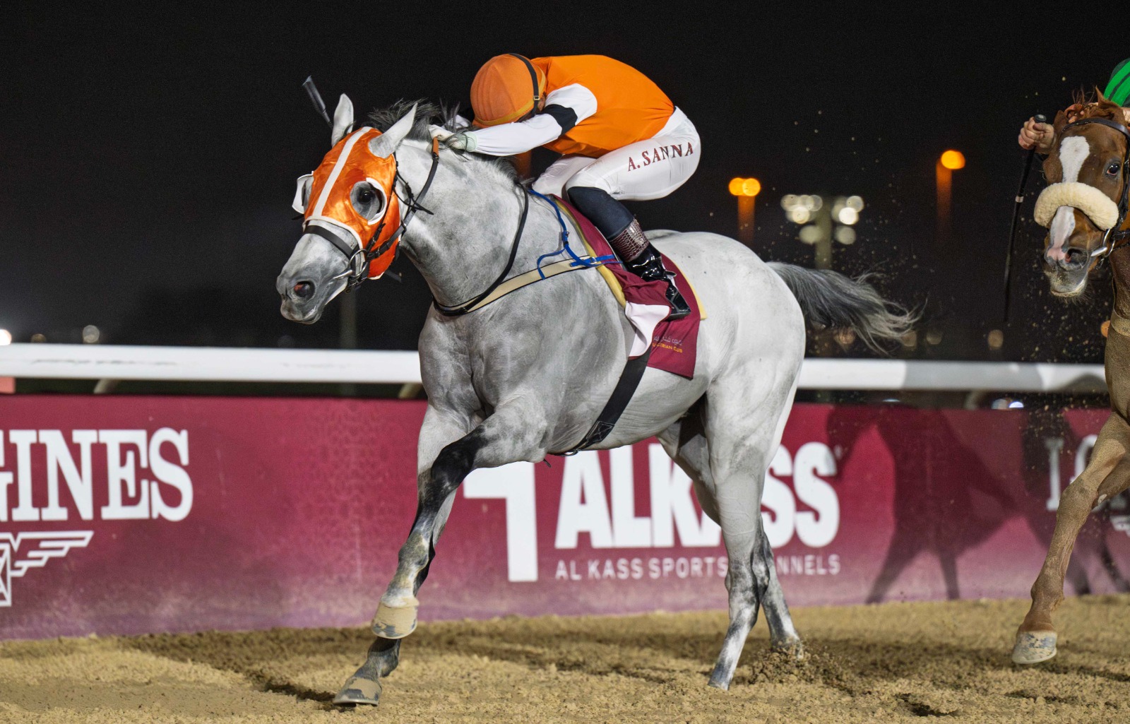 Jockeys racing on dirt track during Al Rayyan Race Meeting at sunset with crowd in background