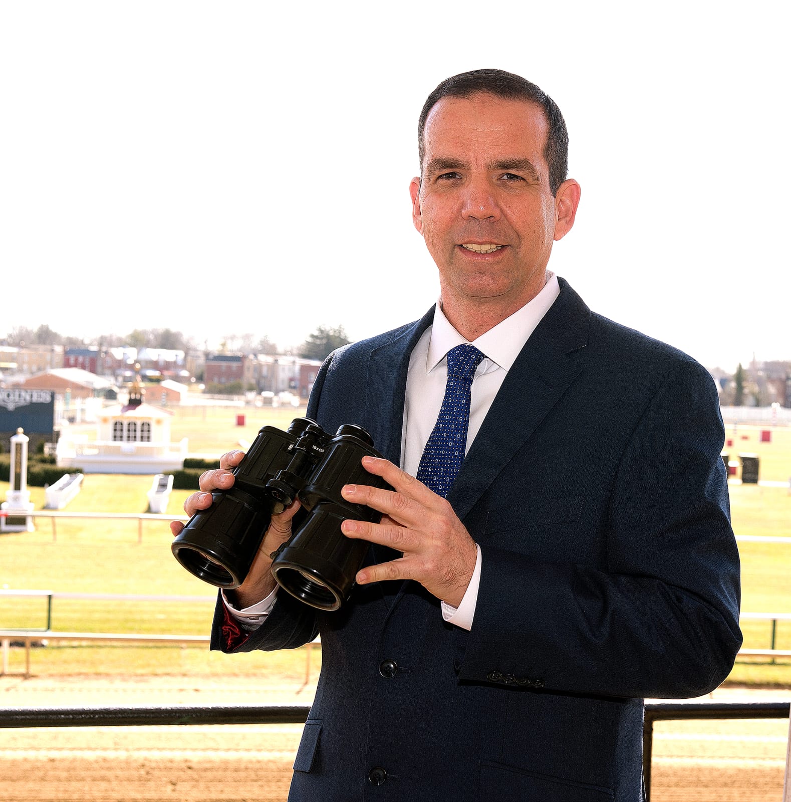 Dave Rodman calling a race at Pimlico Race Course, with grandstands and cheering fans in the background during Preakness Week.