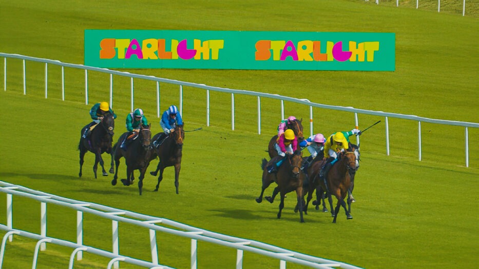 Racehorses in action on the Newbury Racecourse turf during the 2025 Starlight Charity Raceday, with spectators watching in support of children’s healthcare.