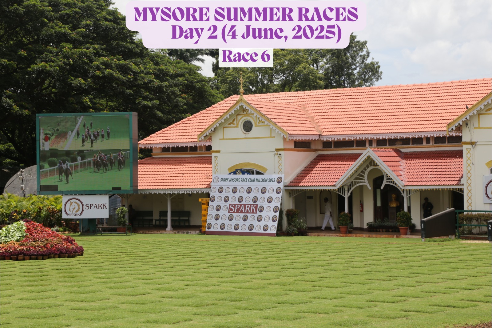 View of the Mysore Race Club finish line during Day 2 of the Mysore Summer Races on June 4, 2025, showing Race 6 signage, colorful flags, and the iconic red-and-white horseshoe arch set against a scenic hill backdrop.