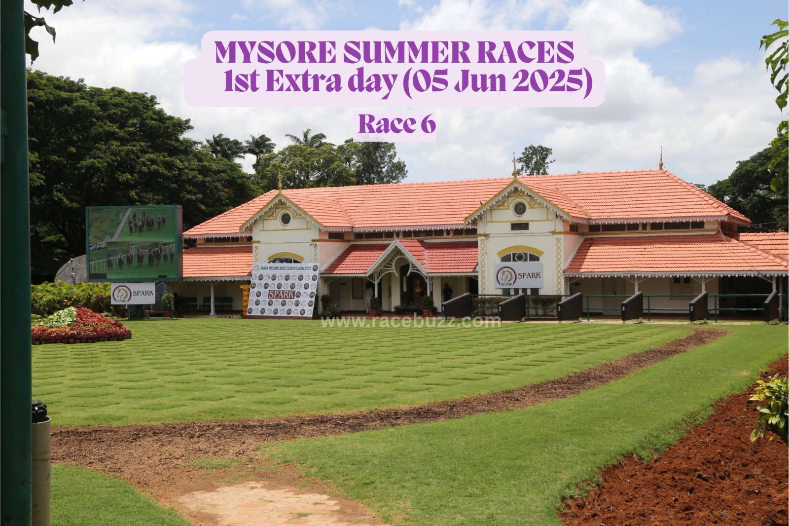 Mysore Race Club paddock area during the Mysore Summer Races 2025 extra race day on June 5, showing the main building, sponsor banners, and a large screen with race footage, set against a clear sky and lush greenery.