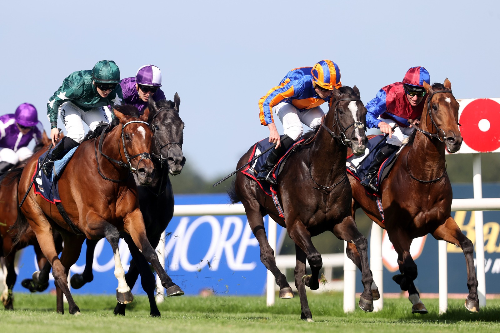 Jockeys in action during a summer evening race at Leopardstown Racecourse, Dublin, with a packed grandstand in the background.