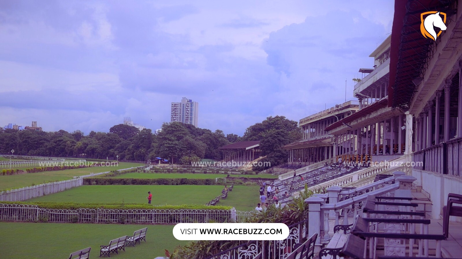 Royal Calcutta Turf Club racecourse with green lawns, seating stands, and colonial-style grandstand under a cloudy sky.