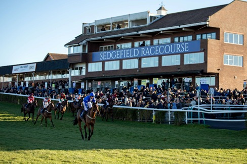 Horses lined up for jump racing at Sedgefield with jockeys